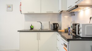 A modern kitchen with white cabinets, a black countertop, a kettle, a microwave, and a sink. - Tanoeiros Studio - Spacious and Comfortable Accommodation (Funchal)