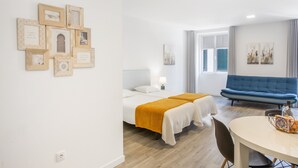A hotel room with two beds, a dining table, a sofa, and wall art. - Tanoeiros Studio - Spacious and Comfortable Accommodation (Funchal)