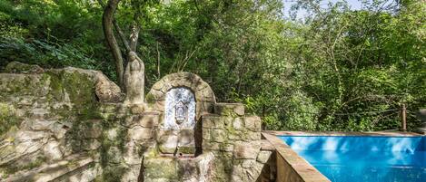 A stone structure with a tiled relief, a pool, and a natural forested backdrop.