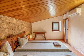A bedroom with a stone wall, wooden ceiling, a bed with pillows, a nightstand with a lamp, and a window. - Eco Masias Cal Ferran Country House with Mountain Views, Wi-Fi, and Air Conditioning (El Bruc)