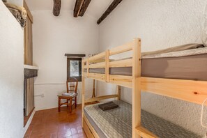 Een slaapkamer met een stapelbed, een houten stoel, een klein raam en een deur.