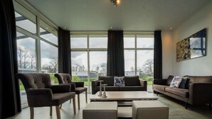 Ein modernes Wohnzimmer mit großen Fenstern, einer Couch, Sesseln und einem Couchtisch.