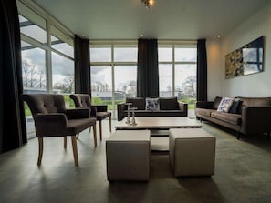 Ein modernes Wohnzimmer mit großen Fenstern, einer Couch, Sesseln und einem Couchtisch.