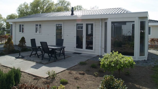Ein Bungalow mit Terrasse, Essbereich mit Stühlen und einem kleinen Garten.