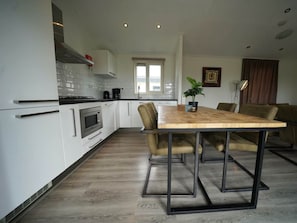 A modern kitchen with white cabinets, a wooden dining table, and a built-in oven. - Holiday Home in Dordrecht With Terrace (Dordrecht)