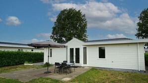 Ein Bungalow mit Terrasse, Tisch und Stühlen, und ein großer Baum im Hintergrund.