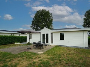 A single-story mobile home with a patio area, a table and chairs, and a large tree in the background. - Holiday Home in Dordrecht With Terrace (Dordrecht)