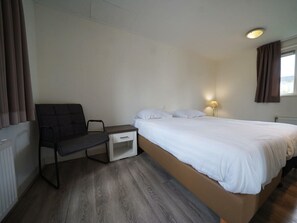 A bedroom with a bed, a chair, a nightstand, a lamp, and a window with curtains. - Holiday Home in Dordrecht With Terrace (Dordrecht)