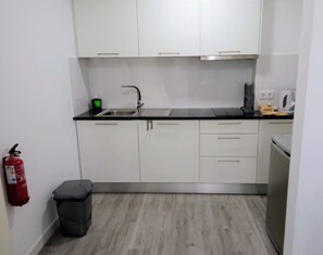 Een kleine keukenhoek met een spoelbak, kastjes, een prullenbak en een brandblusser.