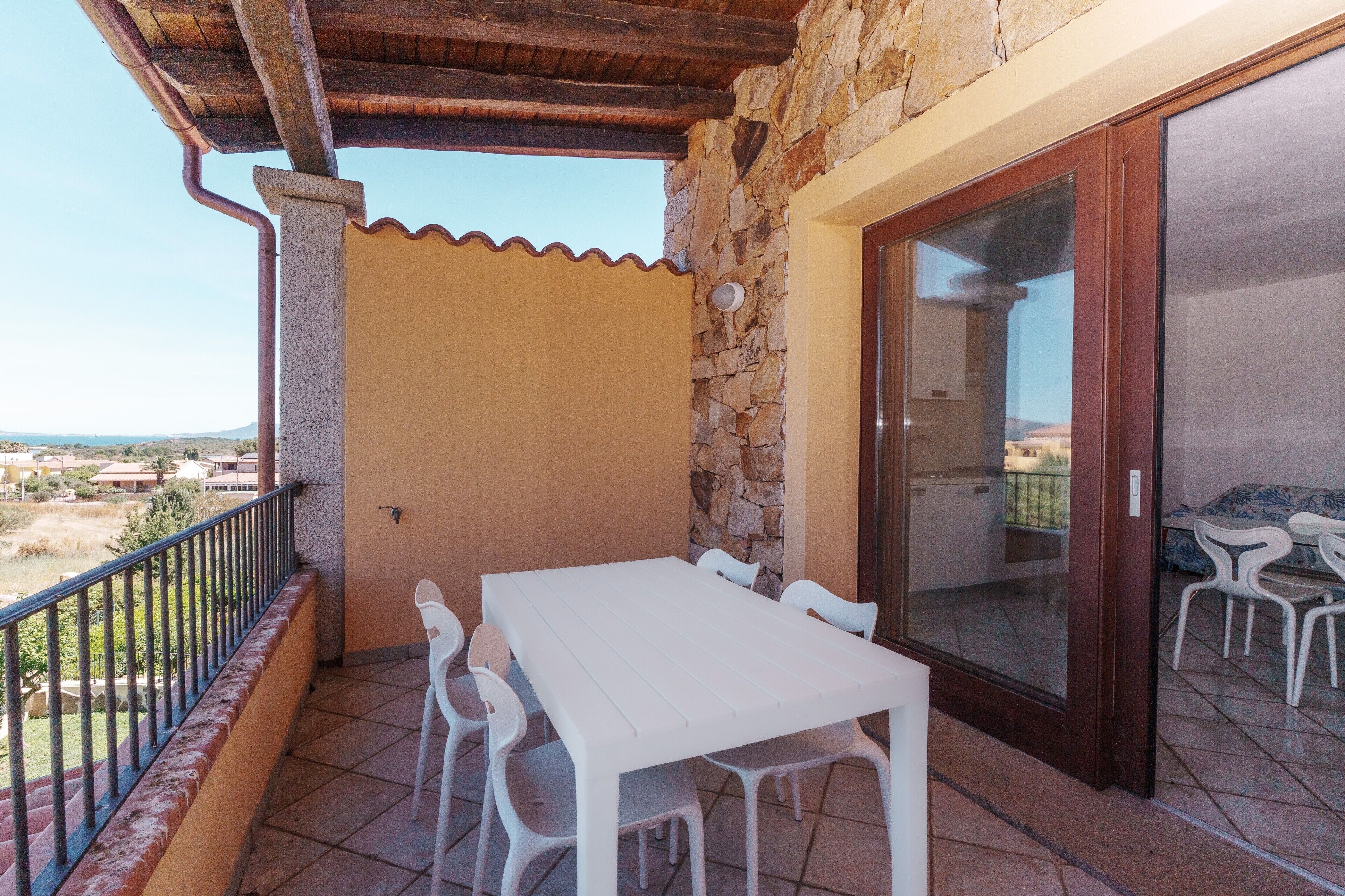 Un balcone con tavolo e sedie bianche, un muro in pietra e vista sul paesaggio.