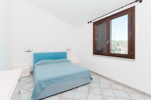 Un dormitorio con cama, ventana y pared blanca.