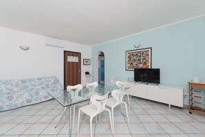 Un comedor con una mesa de vidrio, sillas blancas, un sofá blanco, un televisor y un armario.