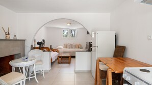 Een compacte keuken met een eethoek, een kleine koelkast en een bed op de achtergrond.