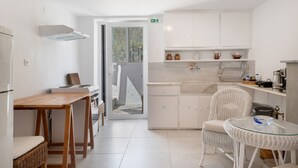 Een moderne keuken met witte kasten, een eethoek met rieten meubilair en een uitzicht door de deur.