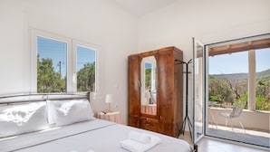 Een slaapkamer met een bed, een houten garderobe, een nachtkastje en uitzicht op de omgeving via een glazen deur.