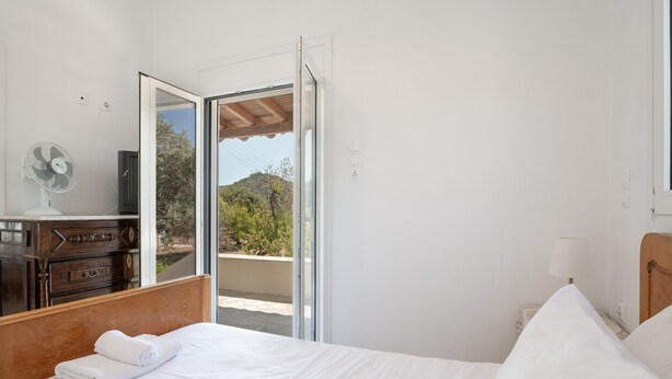 Een slaapkamer met een bed, nachtkastje, dressoir, ventilator en een schuifdeur naar een buiten balkon.