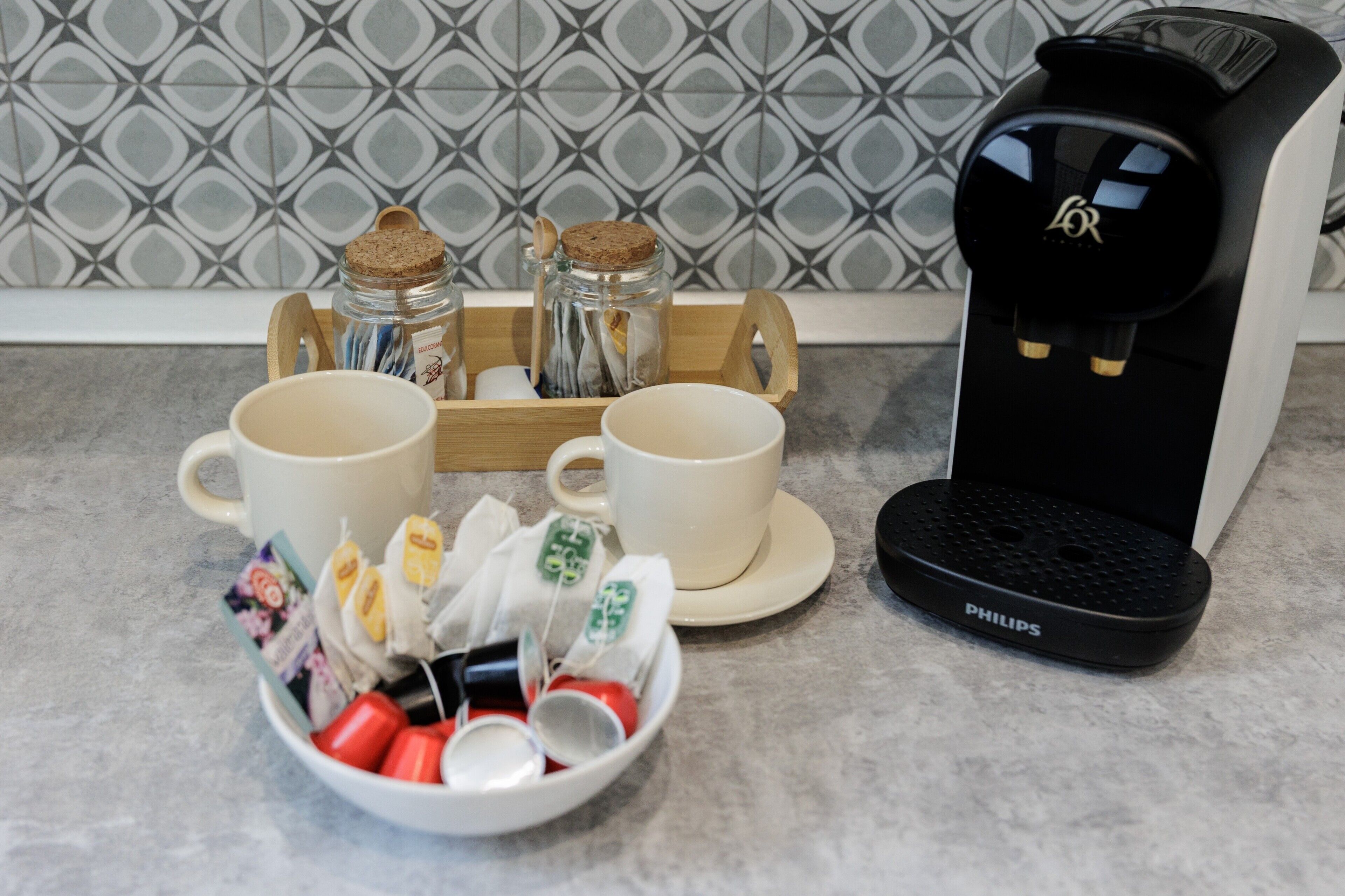 Una cafetera, dos tazas, una bandeja con bolsitas de té y un cuenco con bolsitas y cápsulas.