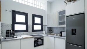 A modern kitchen with two windows, a stainless steel refrigerator, and a tiled backsplash.