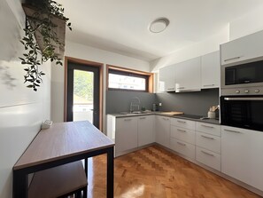A modern kitchen with white cabinets, a built-in oven, and a wooden herringboard floor. - Driftwood – Cozy Retreat Near the Sea (Matosinhos)