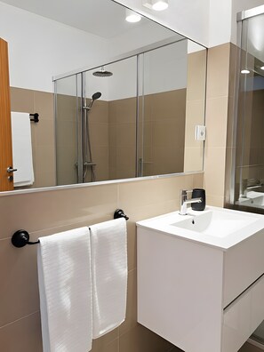 Ein modernes Badezimmer mit Duschkabine aus Glas, einem weißen Waschbecken und einem großen Spiegel.