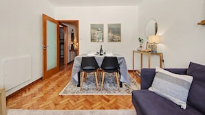 A dining area with a table set for two, a sofa, and a lamp. - Driftwood – Cozy Retreat Near the Sea (Matosinhos)