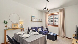 A modern living room with a dining table set for four, a sofa, a TV, and a window with curtains. - Driftwood – Cozy Retreat Near the Sea (Matosinhos)