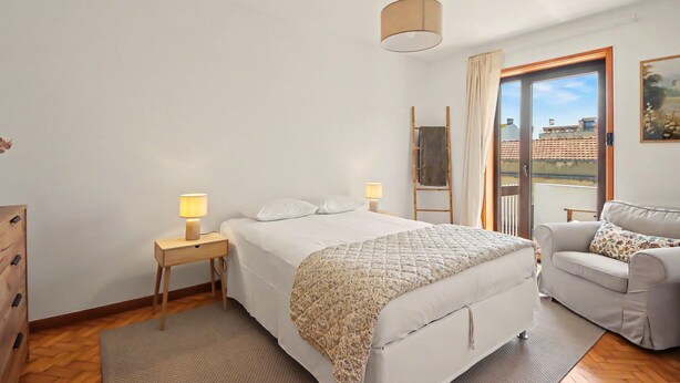 A bedroom with a bed, bedside tables, a sofa, a window with curtains, and a hanging light fixture. - Driftwood – Cozy Retreat Near the Sea (Matosinhos)