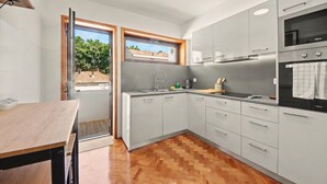A modern kitchen with grey cabinets, a wooden table, and a window with a view. - Driftwood – Cozy Retreat Near the Sea (Matosinhos)