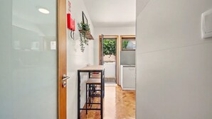 A hallway with a wooden floor, a table with a bench, a hanging plant, and a door leading to a room with a window. - Driftwood – Cozy Retreat Near the Sea (Matosinhos)
