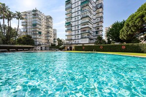 A swimming pool with clear water, surrounded by multi-story residential buildings, palm trees, and a hedge. - Apartment 'Copenhague - 049' with Mountain Views, Wi-Fi, and Air Conditioning (Torre del Mar)