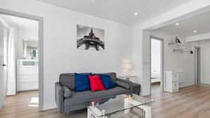 A modern living room with a glass coffee table, grey sofa with red and blue cushions, a wall-mounted picture of the Eiffel Tower, and a white desk with shelves. - Apartment 'Copenhague - 049' with Mountain Views, Wi-Fi, and Air Conditioning (Torre del Mar)