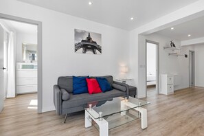 A modern living room with a glass coffee table, grey sofa with red and blue cushions, a wall-mounted picture of the Eiffel Tower, and a white desk with shelves. - Apartment 'Copenhague - 049' with Mountain Views, Wi-Fi, and Air Conditioning (Torre del Mar)