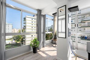 A modern apartment with large windows, a potted plant, and a view of neighboring buildings.