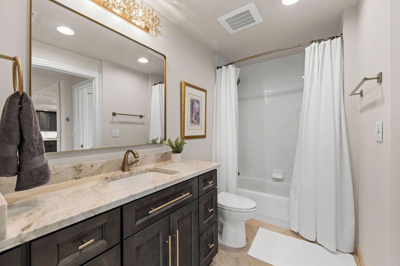 Une salle de bain moderne avec un lavabo en marbre, des meubles sombres, un grand miroir, des toilettes blanches et une douche à parois de verre.
