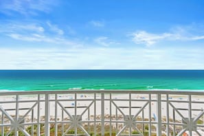 Blick auf den Strand vom Balkon aus, mit Geländer, Meer und blauem Himmel.