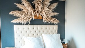Ein Schlafzimmer mit einer gesteppten Kopfteil, weißer Bettwäsche, einem Holznachttisch und einer großen Zimmerpflanze.