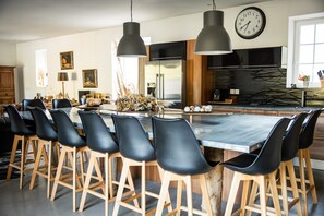 Eine moderne Küche mit einer großen Kochinsel, Barhocker, Pendelleuchten und einer Uhr an der Wand.