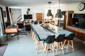 Eine moderne Küche mit einer großen Kochinsel, Barhocker, einem Tischfußballtisch und einem Essbereich mit einer Couch und Sesseln.