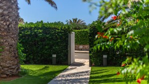 A pathway leading through a lush garden with a stone wall and a palm tree. - Holiday Home 'Villa Jaume' with Private Pool, Private Garden and Air Conditioning (Cap d'Artrutx)