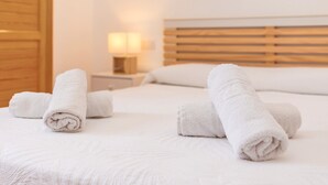 A neatly made bed with rolled white towels, a wooden headboard, and a bedside lamp. - Holiday Home 'Villa Jaume' with Private Pool, Private Garden and Air Conditioning (Cap d'Artrutx)