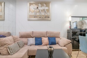 Een moderne woonkamer met een beige bank, gekleurde kussens, een zwarte salontafel en een schilderij van dansers.