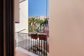 A balcony with a railing, potted plants, and a view of buildings in the background.