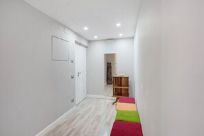Käytävä, jossa on valkoinen ovi, peili, puinen hylly ja värikäs matto.