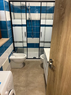 Un bagno con doccia, due servizi igienici, un lavandino e una lavatrice.