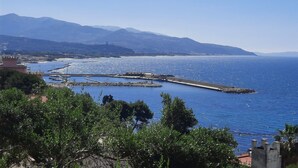 A coastal view with a marina, mountains in the background, and greenery in the foreground.