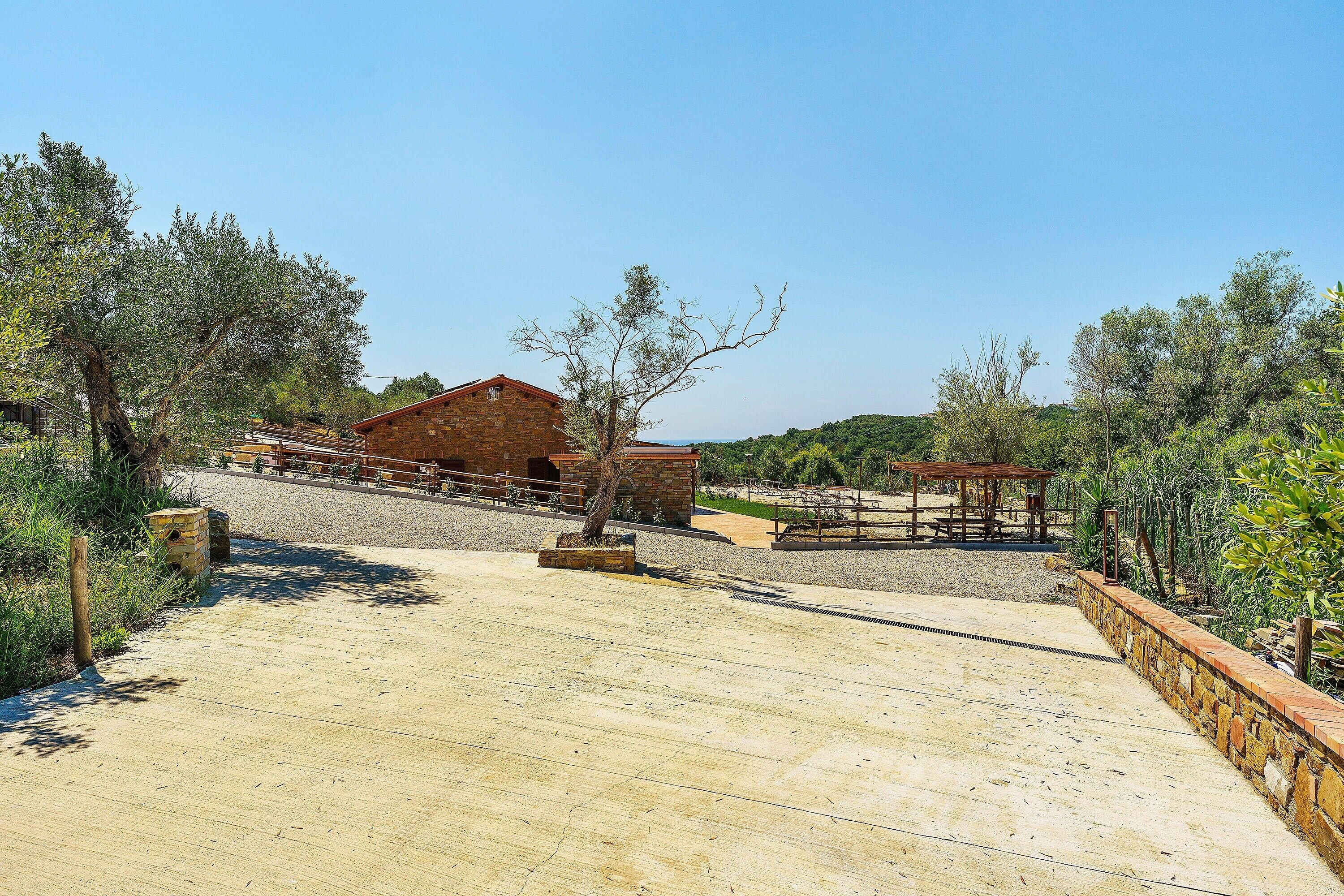 A paved pathway leading to a rustic building with a wooden fence and a small structure in the background.