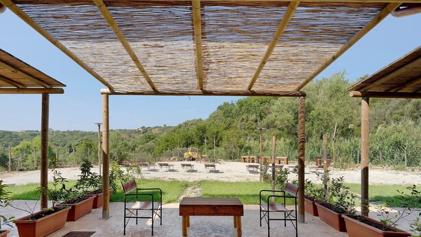 A covered outdoor seating area with a table and chairs, surrounded by planters and a view of a construction site.