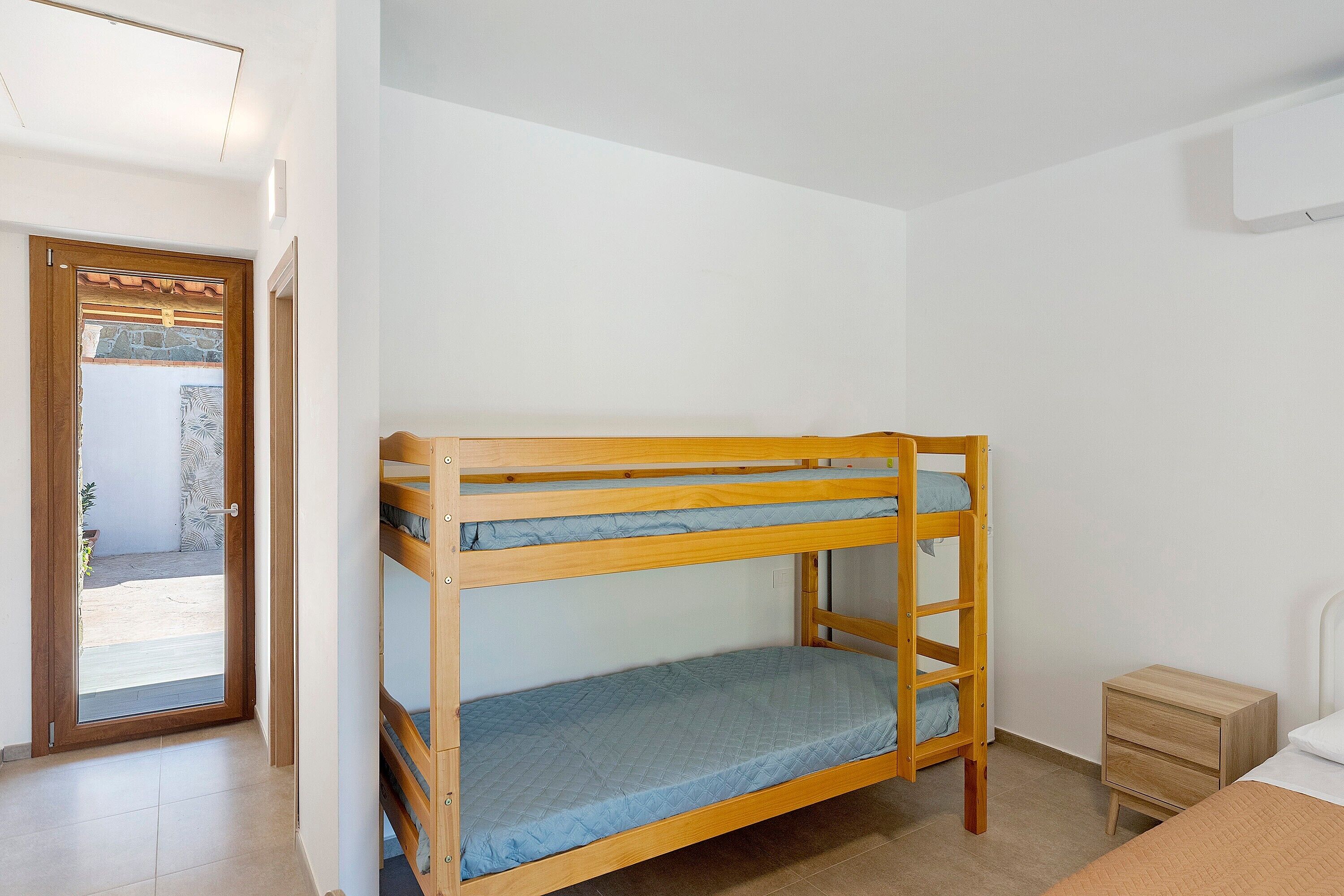 Ein Stockbett mit Holzrahmen, ein kleiner Nachttisch und eine Tür zu einem Außenbereich.