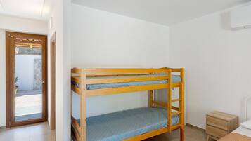 Ein Stockbett mit Holzrahmen, ein kleiner Nachttisch und eine Tür zu einem Außenbereich.