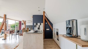 Una cocina moderna con una isla central, vigas de madera y una cafetera sobre un estante de madera.